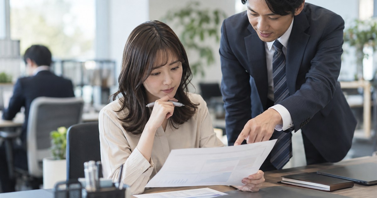 印刷した原稿を確認する担当者と、横から紙面を指さす営業担当者