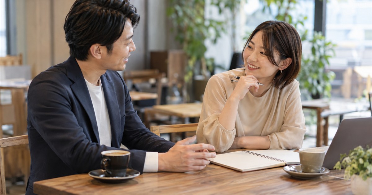 ノートとコーヒーを置いたテーブルで制作範囲を相談する担当者と編集者