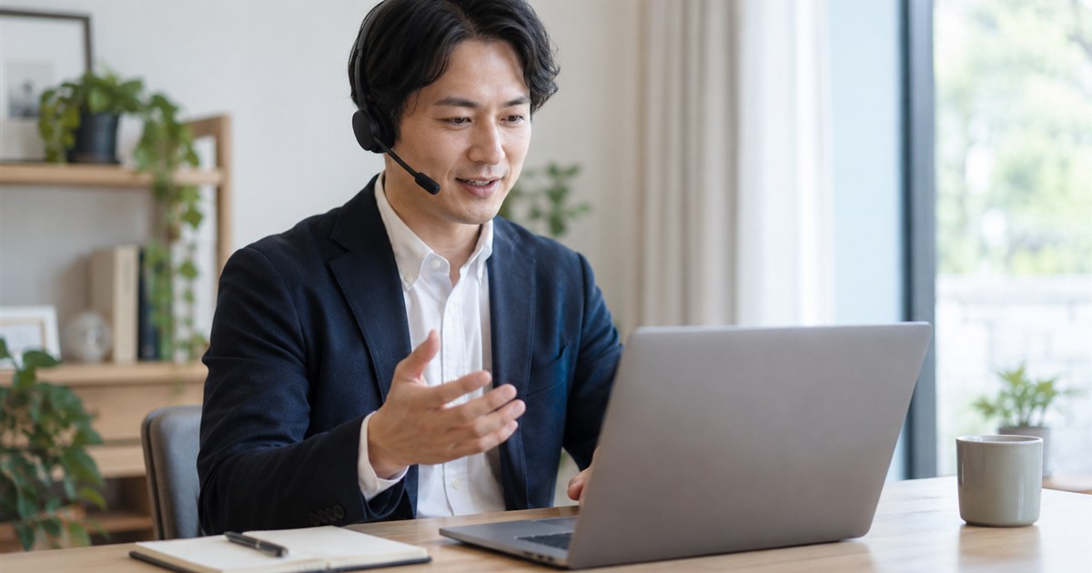 ノートパソコンの前でヘッドセットを付け、オンラインで打ち合わせをする日本人のビジネスパーソン