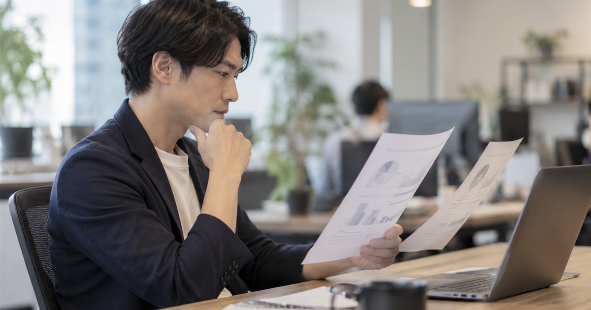 オフィスの机で2冊の提案書を見比べるマーケティング担当者