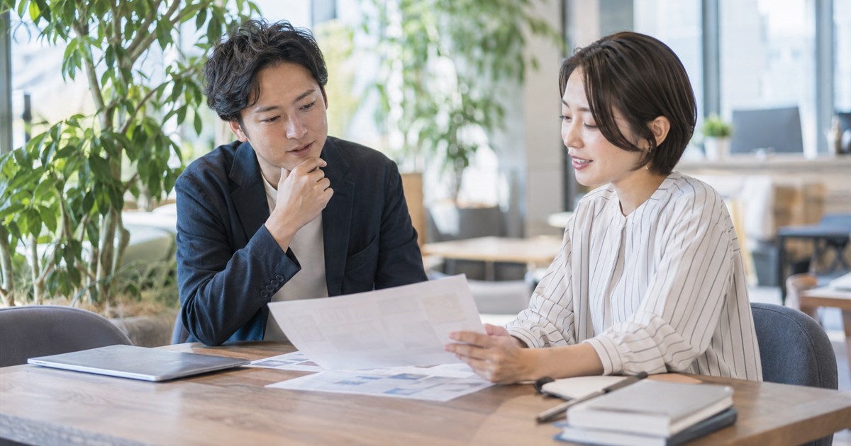 明るい打ち合わせスペースで、印刷した構成案を前に相談する二人の担当者