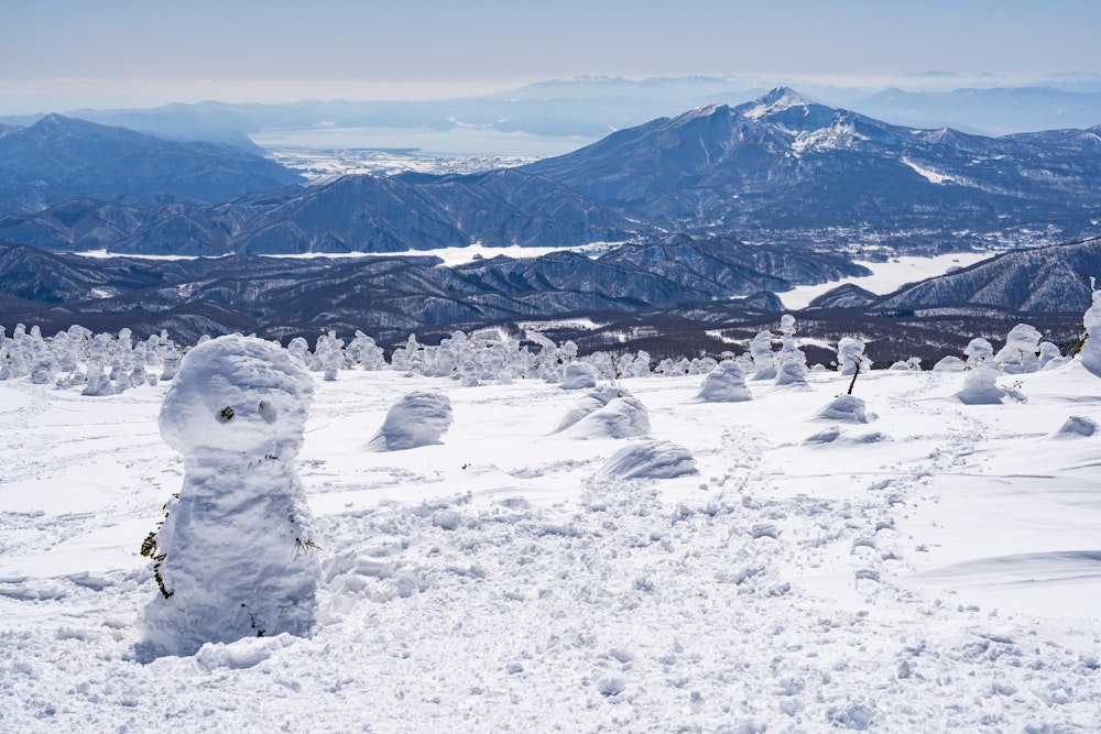 <p>西吾妻山の頂上は分厚い積雪で山頂標識は埋もれている。<br>代わりにスノーモンスターの雪だるまが出迎えてくれた。<br>その向こうには磐梯山や猪苗代湖が見える。</p>