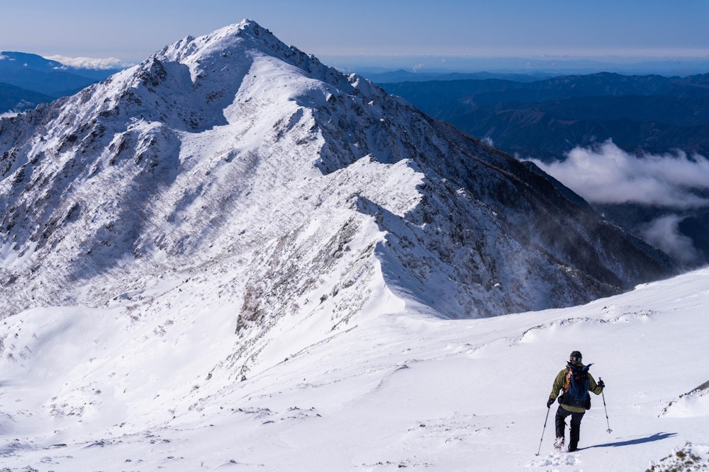 <p>極楽平に出ると、三ノ沢岳が目の前に突如として現れる。思ったよりも大きく下って登り返すようだ。<br>昨日の降雪で新雪がしっかりついている。ところどころ歩きづらい。</p>