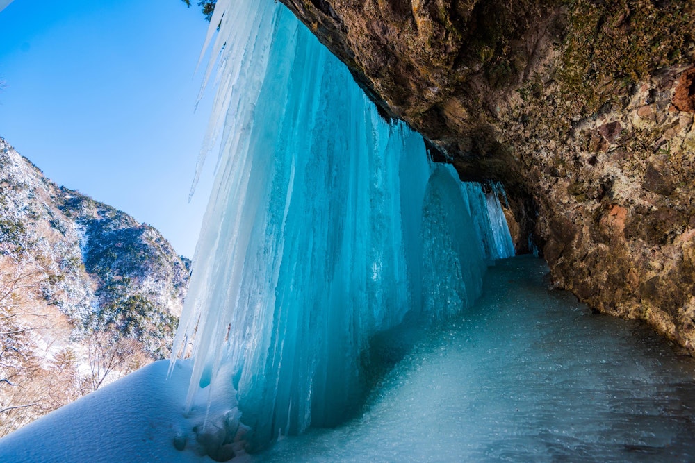 <p>庵滝の面白いところは、こうして裏側に入り込むことができる。<br>しかし氷瀑とあって、付近の地面を覆っているのは雪ではなく完全なる氷。<br>傾斜のあるスケートリンクのようなものなので、アイゼンを履かなければとても歩き回れない。</p>