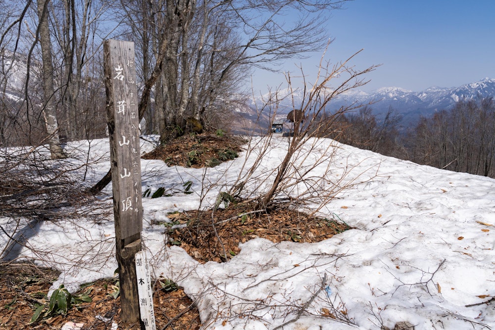 <p>山頂標識は樹林帯のこじんまりとした場所にある。<br>ここから白馬連峰はあまり見えないが、北の方向には頸城山塊が遠望できる。</p>