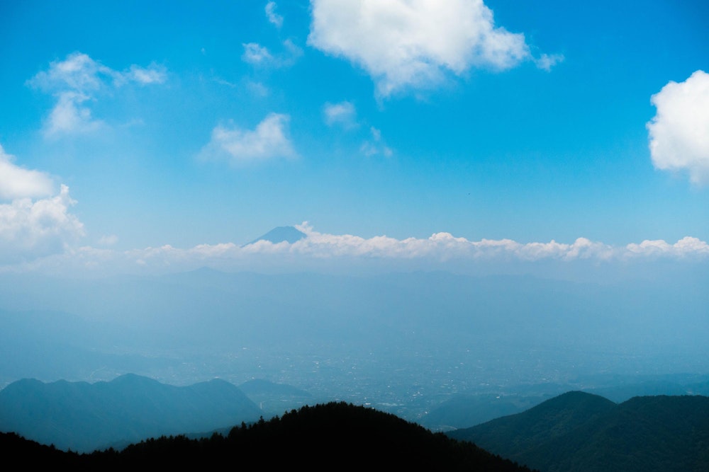 <p>少し霞んでいるが、雲の上に顔を出す富士山の姿が見える。</p>