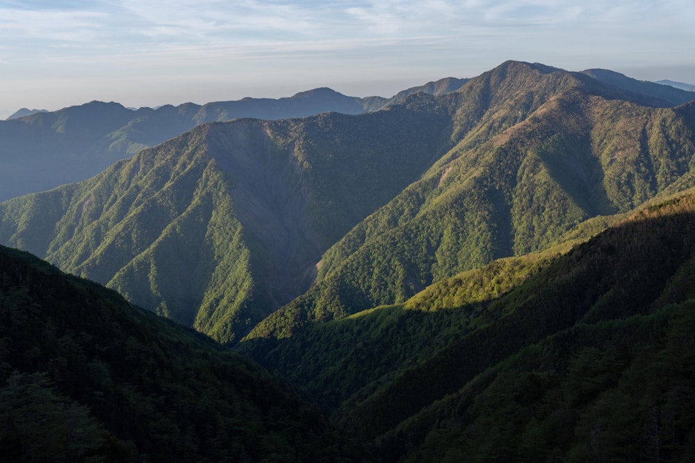 <p>翌朝、布引山を登りながら後ろを見ると、朝日に浮かぶ青笹山が見えた。<br>昨日その頂を踏んだ青薙山と隣り合う青笹山だが、その間には青薙崩と呼ばれる崩壊地があり、そこはもはや通行できないとされている。<br>近くて遠い山。</p>