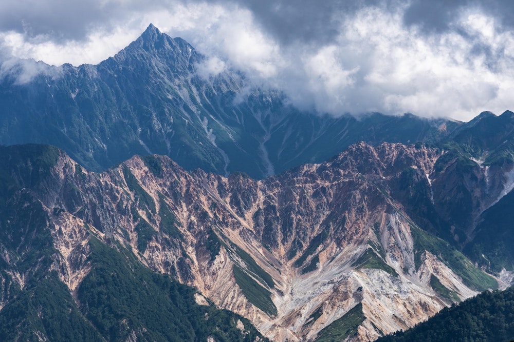 <p>雲に隠れて見えなくなっていた槍ヶ岳が、一瞬だけその姿を現した。穂先以外の稜線は雲に隠れている。</p>