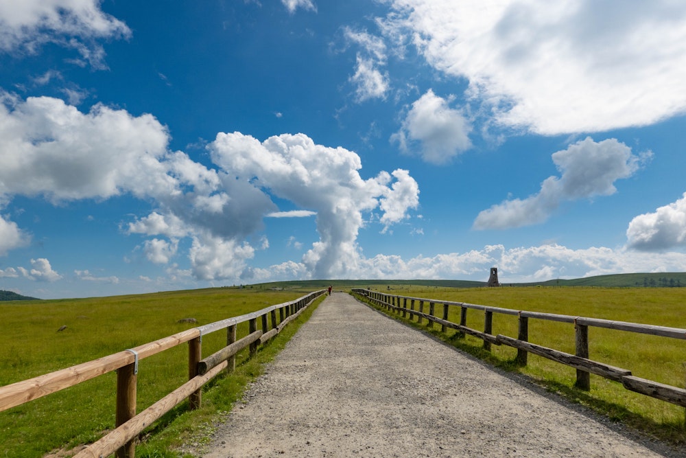 <p>美ヶ原とは、広大でほとんど標高差のない 2000m 前後の台地状の地形となった高原地帯である。<br>青空と夏の雲が、緑の牧草地によく映える。<br>写真の遊歩道は、車も通る道になっており、王ヶ頭ホテルの送迎バスと何度かすれ違った。</p>