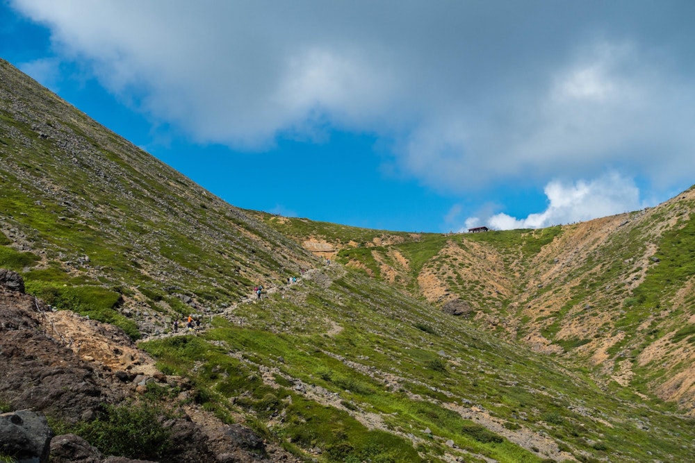 <p>しかしすぐに景色がひらけてくる。<br>山腹のトラバース道を抜けた先に見えるのが、峰の茶屋跡避難小屋。<br>あそこが茶臼岳と朝日岳の分岐になっている。</p>