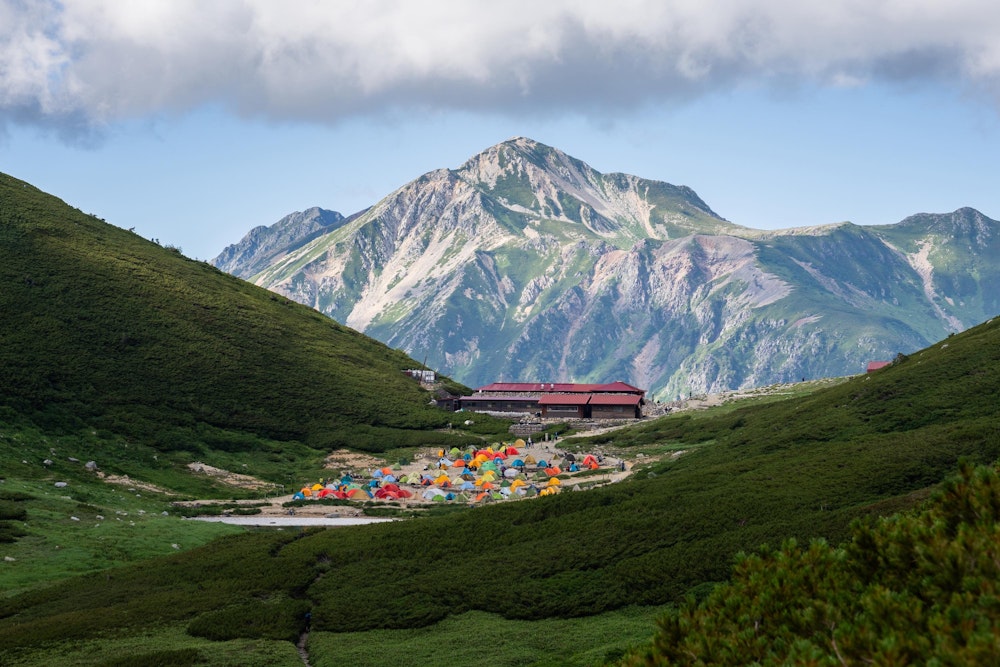 <p>双六小屋とカラフルなテントが見えると同時に、その向こうには真正面に端正な山容の鷲羽岳が覗く。</p>