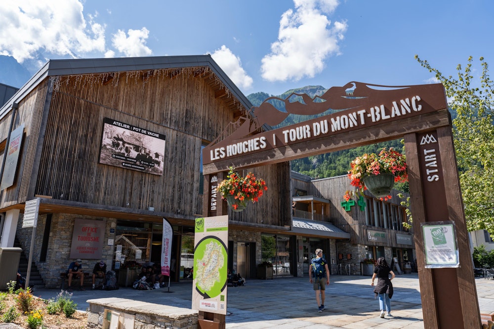 <p>シャモニーで１泊し、現地入り翌日がトレッキング初日。<br>Les Houches（レ・ズーシュ）まで送迎車で移動すると、ツールドモンブランのスタートゲートがある。<br>ここは記念撮影のためだけに立ち寄り、今回のツアーハイキングの起点はまださらに少し先となる。<br>ちなみにゴールゲートはないそう（TMB は一周のトレイルなので、スタートゲートに戻ってくることがすなわちゴールだからか）</p>