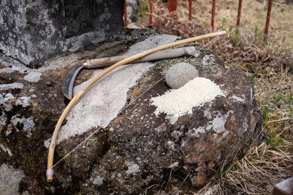 <p>守屋神社奥宮の祠の前に捧げられた鎌・弓・米・石。<br>雨乞いと五穀豊穣の信仰の象徴。</p>