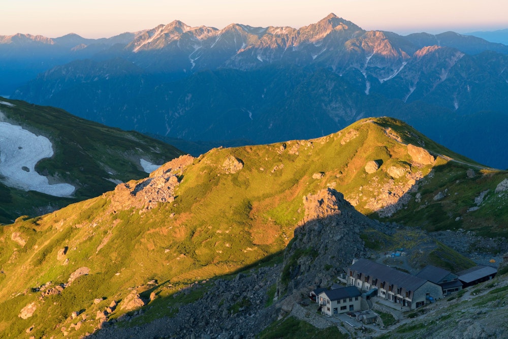 <p>モルゲンロートの立山連峰。右端の剱岳がよく目立つ。<br>右下には村営頂上宿舎が見える。</p>