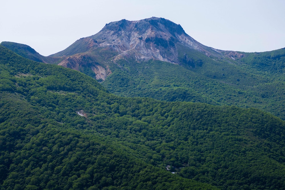 <p>裏那須というだけあって、那須岳の主峰ともいえる茶臼岳の姿をここからも見ることができる。<br>付近の山はほぼ全体が深い緑で覆われているにもかかわらず、この茶臼岳だけは植物を寄せ付けない無骨な活火山の姿をしており、ひときわ目立っていた。</p>