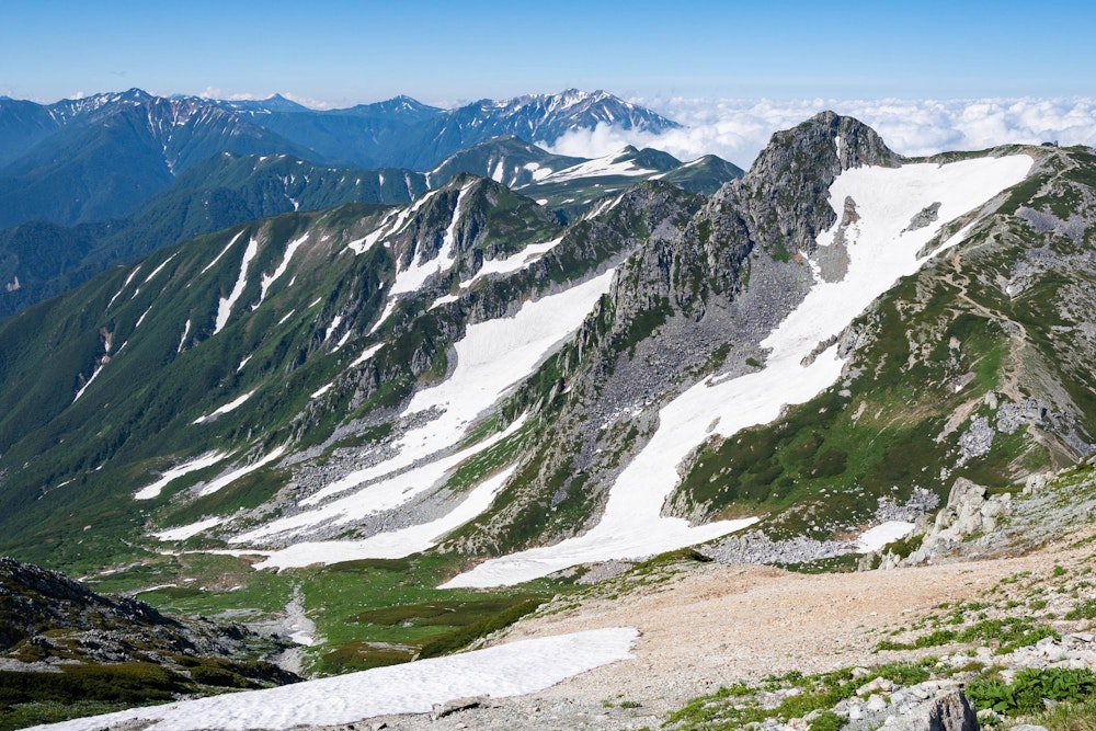 <p>北アルプスの南方面に連なる山々。主に薬師岳方面の景色。<br>北アルプス北部は特に雪深いところで、7 月末でもこれだけ雪渓が残っている。</p>