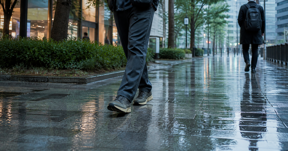 雨上がりの街の歩道を歩く、日常的な服装とスニーカーの足元