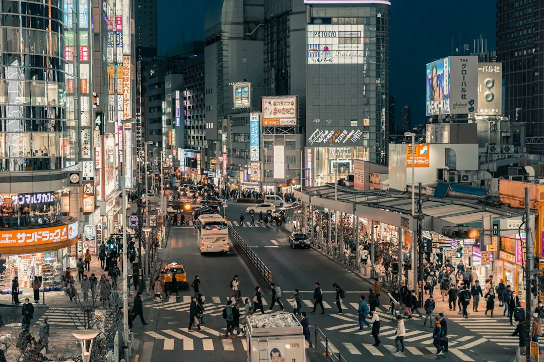 夜の東京の繁華街。ビルの看板や大型ビジョンが並ぶ通りを多くの人が行き交う