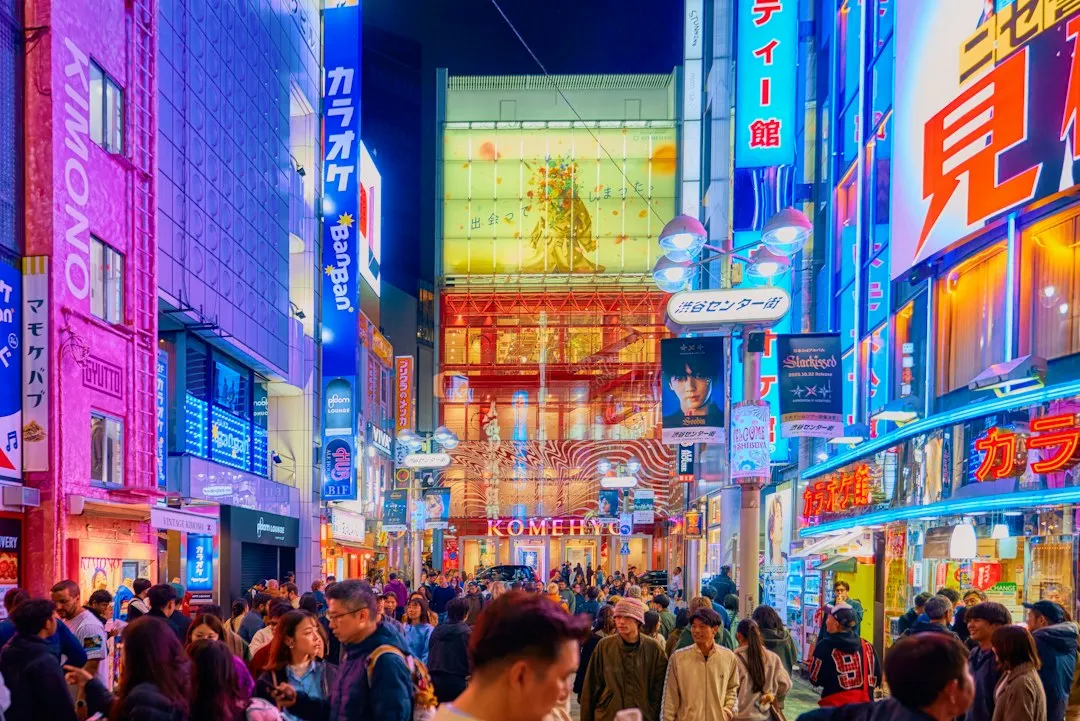 夜の東京の繁華街。映画館や映画の看板が並び、多くの人が行き交う様子