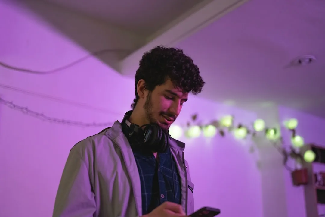 ヘッドフォンをしながらスマートフォンでゲームをプレイする若者」 width=