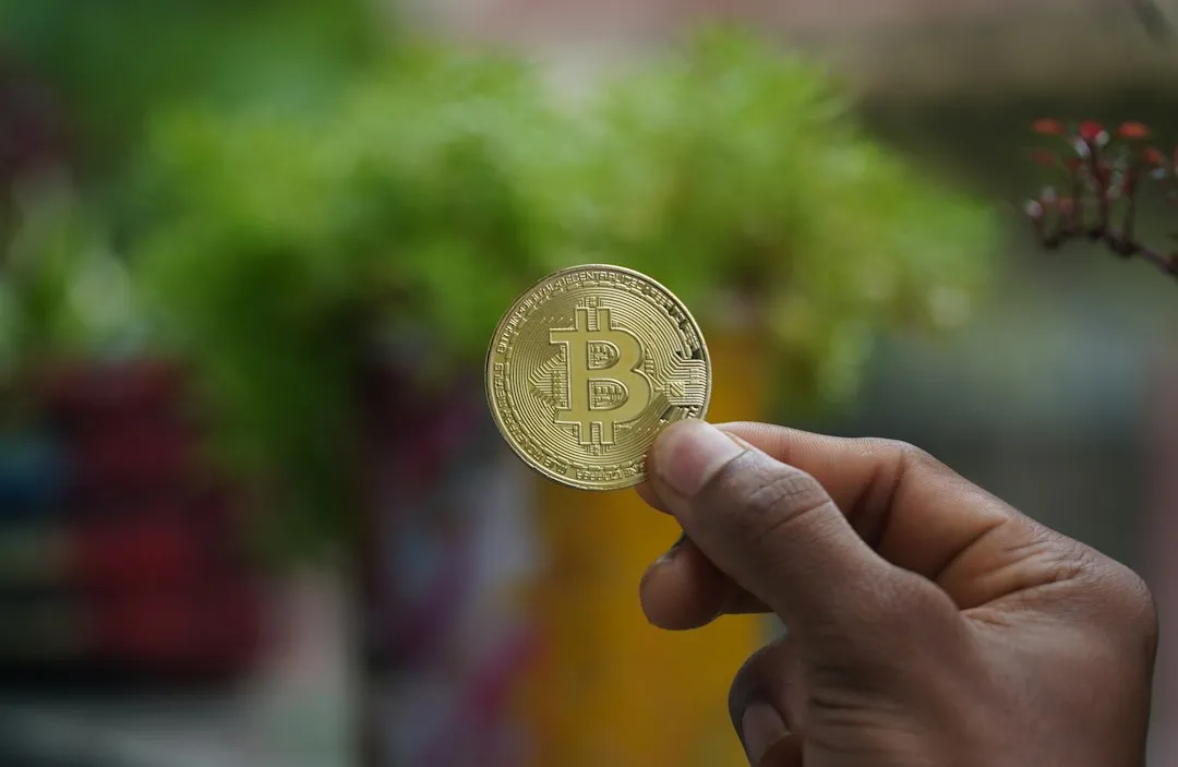 ビットコインの金色のコインを指でつまんで見せる手元