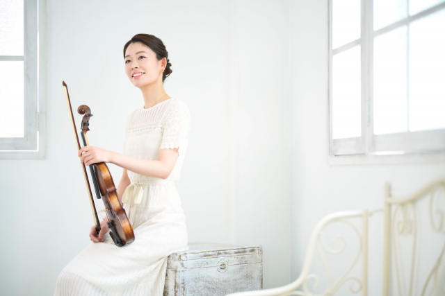 バイオリンを持って窓辺に座る白い服を着た女性