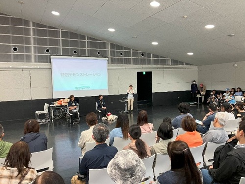 Three staff members talking in front of large audience at the event hall.