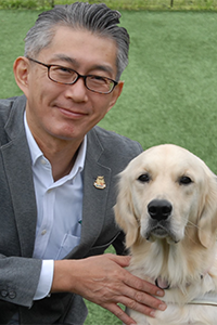 Manabu in a suit, with a golden retriever in a harness.