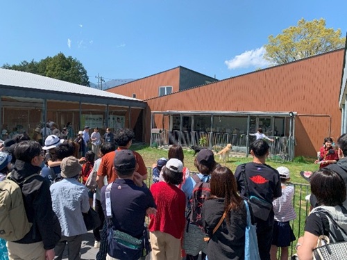 Visitors are standing around the grass free run space and listening to the staff.