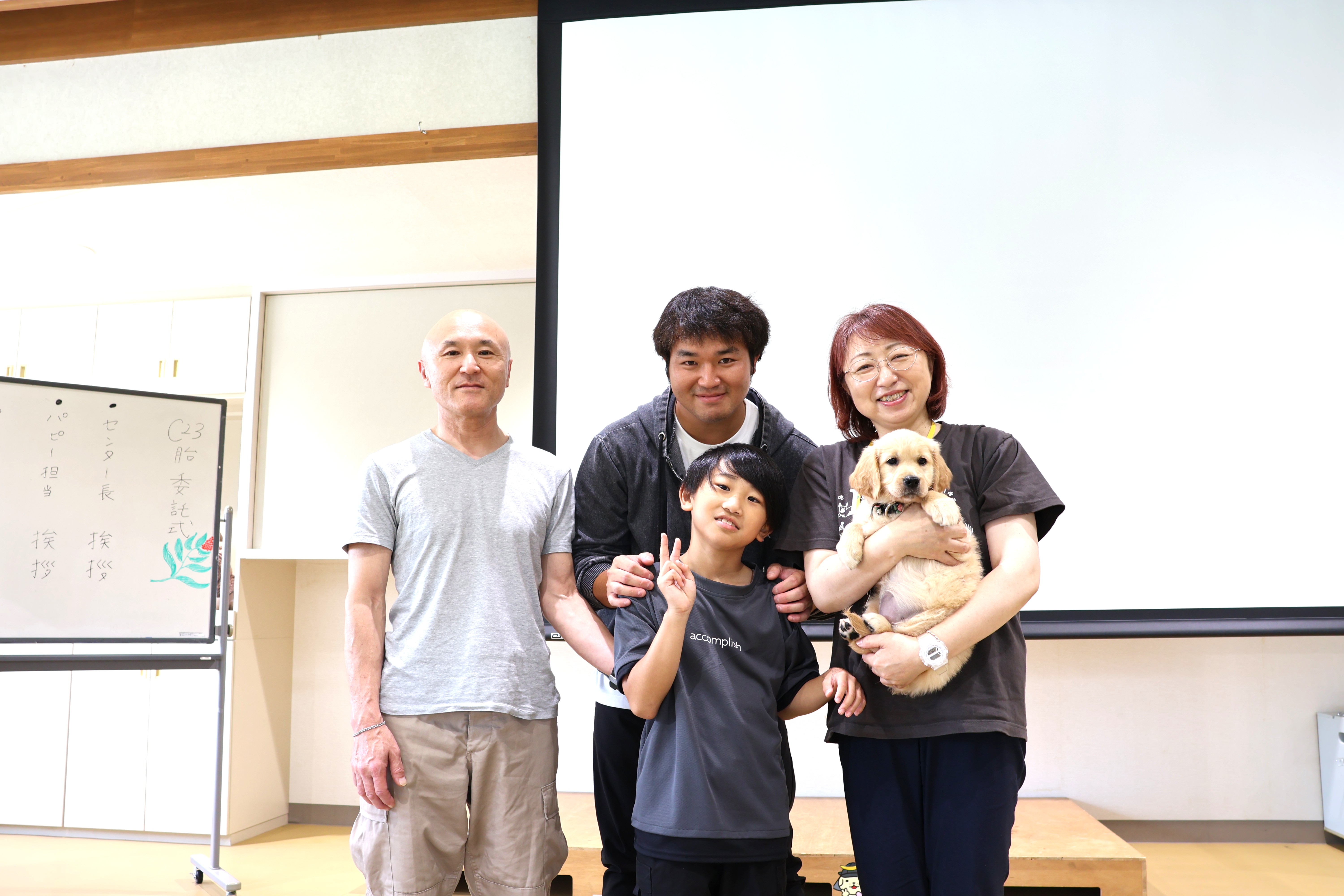 Group photo of Ms S’s family: Ms. S, her husband, son, and grandchild smiling alongside the puppy