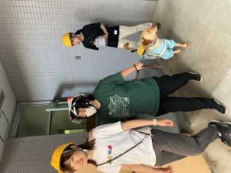 JGDA guide dog user staff wearing a white collapsible helmet and her yellow lab guide dog is guided by a another staff wearing a yellow hard helmet towards the emergency exit.