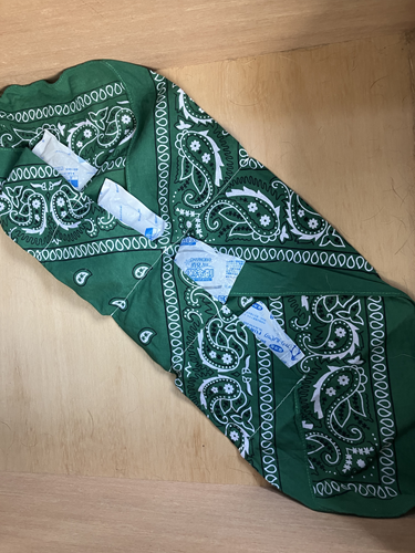 A green scarf is laid on the table, showing cooling gel packets in the pockets. 