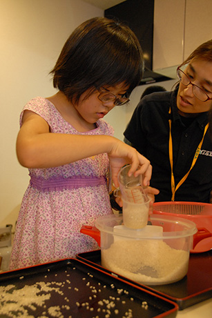 A girl is measuring rice using a cup with the assistance of a staff member.