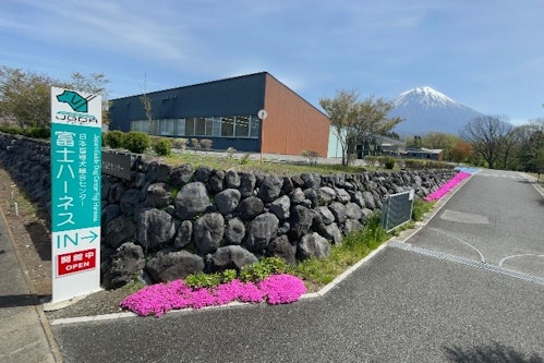 Emerald green JGDA signboard stands along the road by the gate of Fuji Harness.
