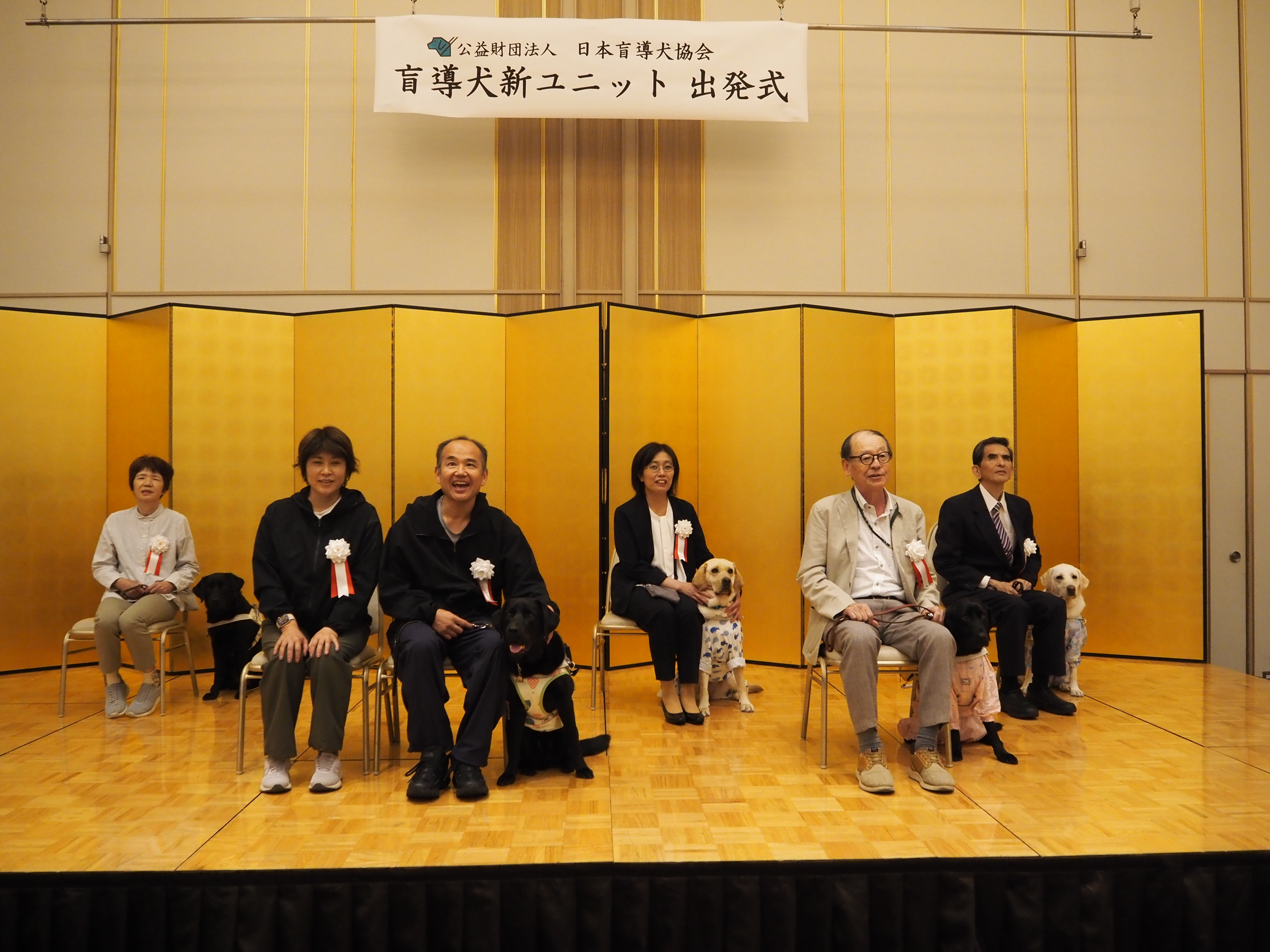  Five Guide Dogs and Six Clients from the Chugoku and Shikoku Regions sitting on stage.