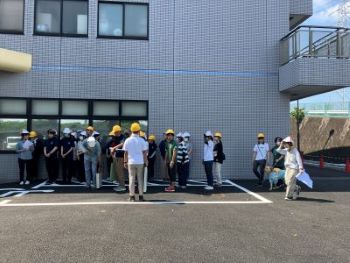 JGDA staff wearing white and yellow helmets are gathering at a safe place outside the building.