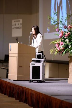 Dr Asakawa presenting at the podium with the actual AI suitcase by her side on stage 