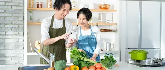 スマホでレシピを見ながら料理をするカップル