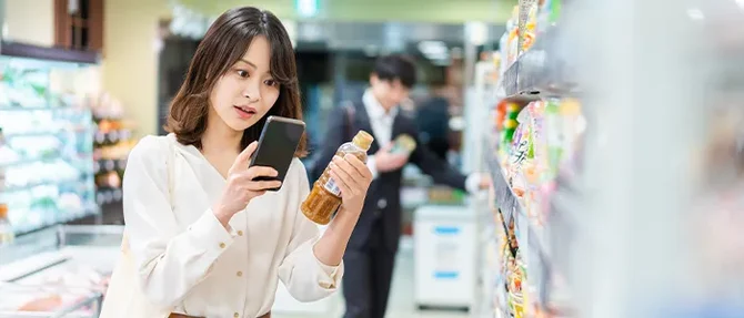 アプリの広告を見ながら商品を選ぶ買い物客