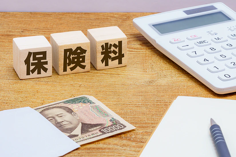 「保険料」という文字の描かれた積み木の側に、お札と電卓、ボールペンが置いてある画像