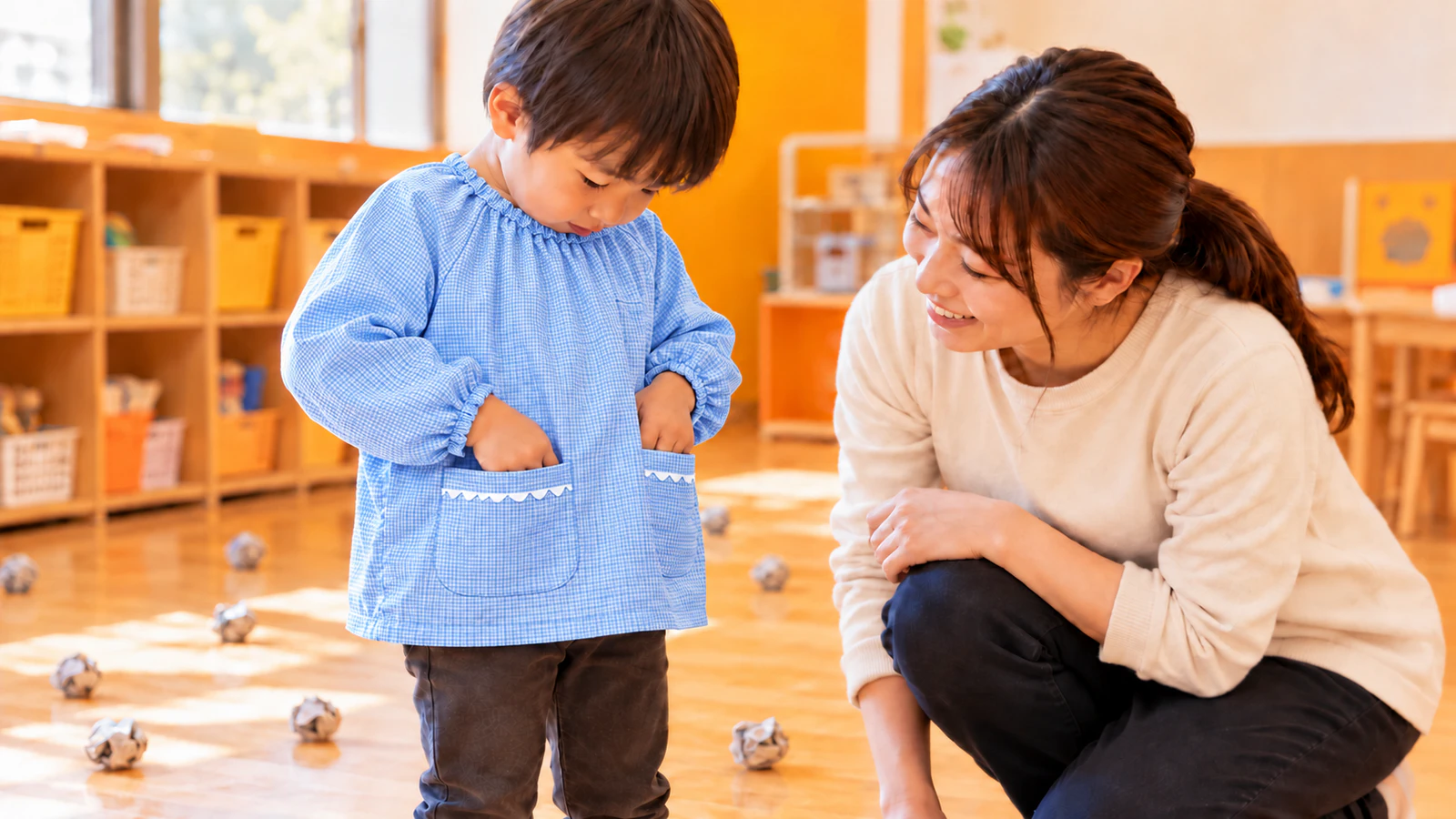豆まきの後、スモックを着た子どもが先生と一緒に、スモックのポケットの中に豆が残っていないかを確かめている様子