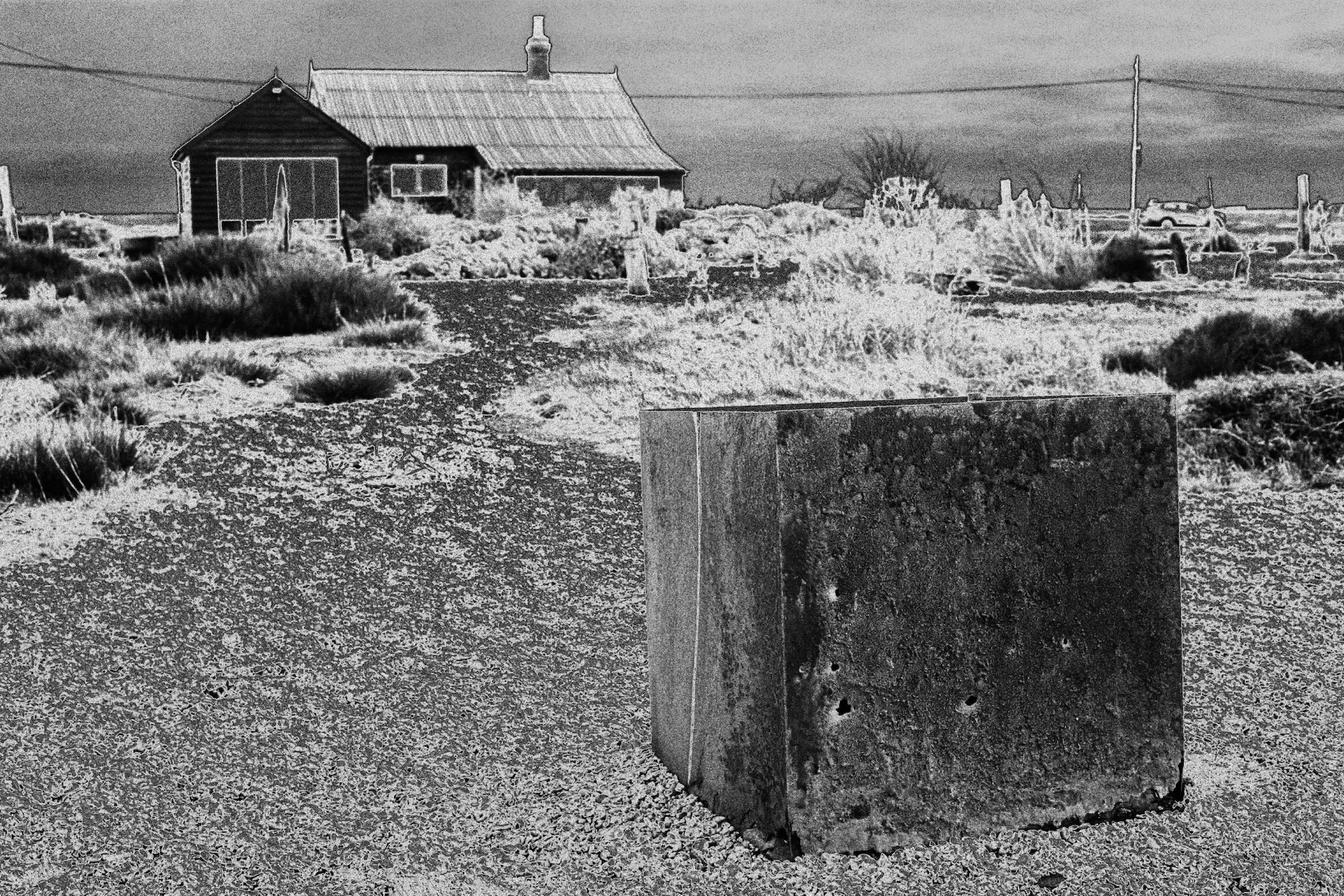 A photo covering a double spread in “Samsara.” There is a house in the background. In the foreground is what appears to be a large, square metal box.