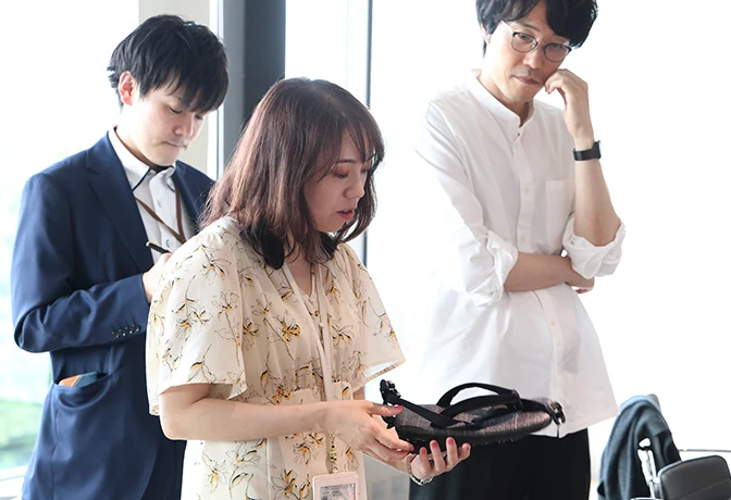 A photo of Japan Pavilion staff members holding uniform samples and as they listen to an explanation.