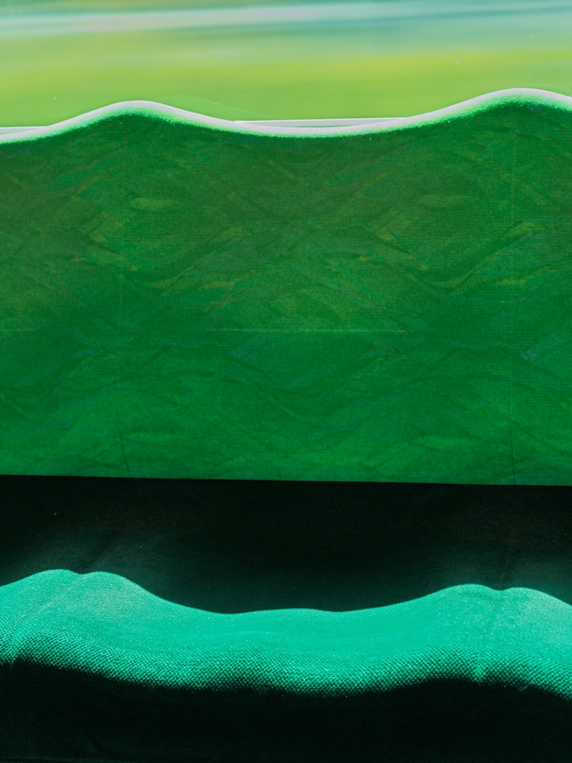 A close-up photo of an object with a green waveform pattern. The waveform stands out on the light green background at the top, and the waveform appears on the dark background at the bottom. These are in fact parts of train seats that were photographed.