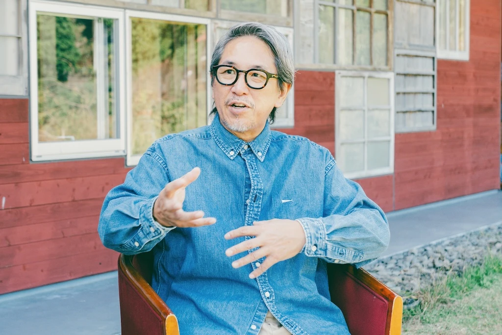 Photo of Mr. Tanaka. He is sitting in a chair talking.