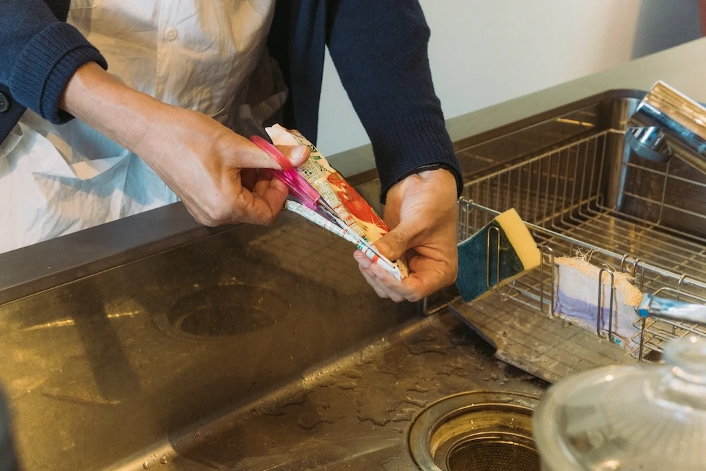 A hand-held photo of a paper juice carton being cut in the sink.