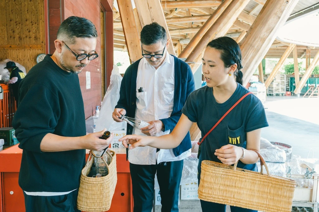 Photos of Mr. Irobe staring at a clear bottle with a label attached, Mr. Watanabe taking a brown bottle out of the basket and staring at it, and Ms. Otsuka and others looking like they are explaining something to Mr. Watanabe.