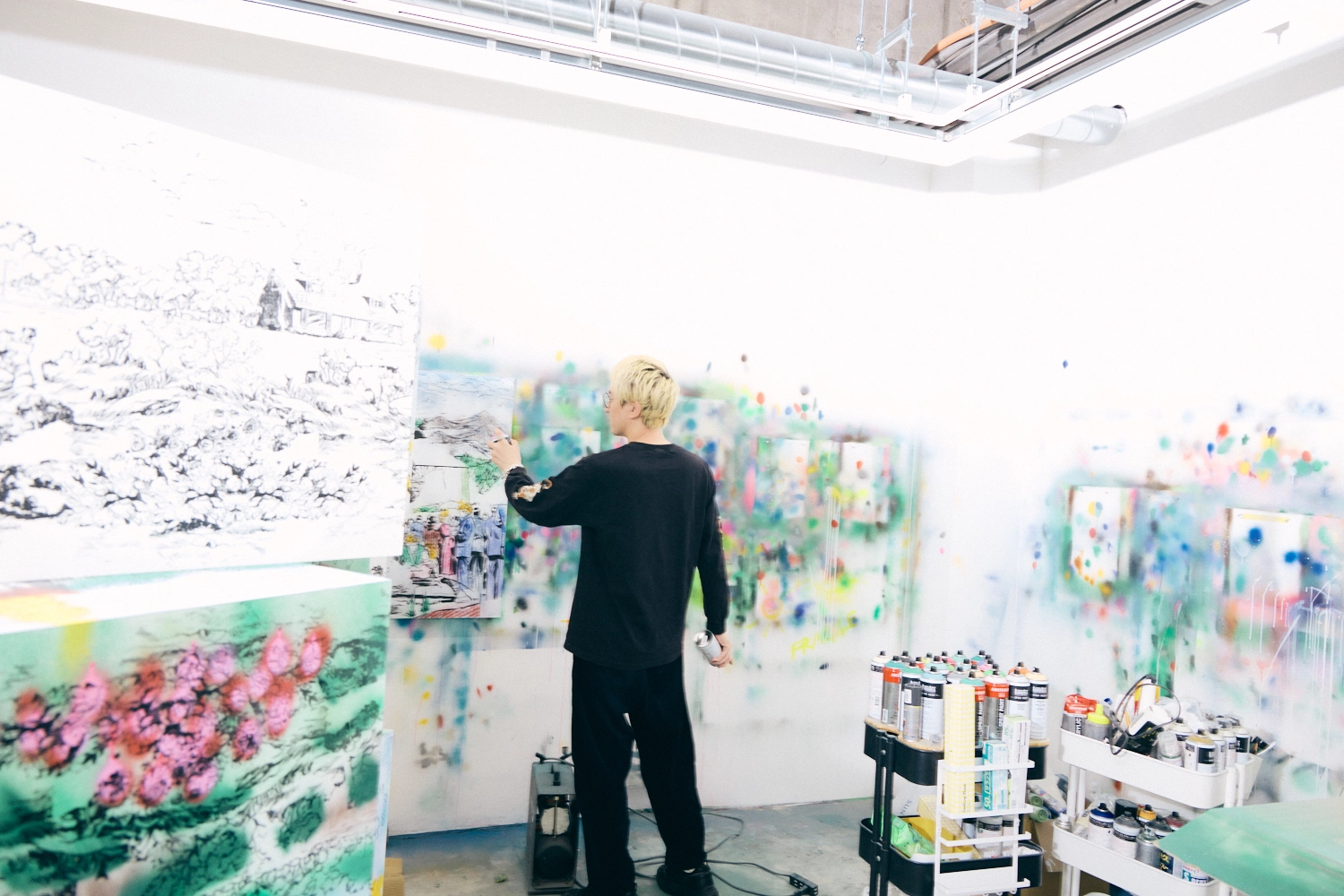 A photo of Hiroki Niimi working in his studio. He is holding spray bottles in both hands and using the one in his left hand to add color. Part of the artwork is visible in the foreground.