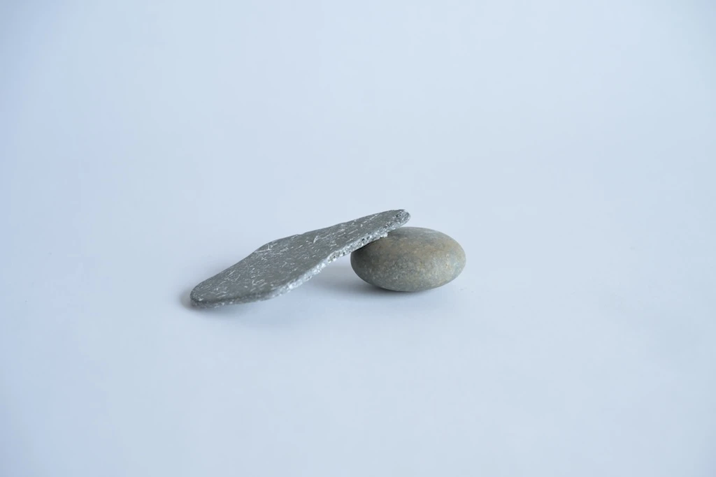 Photo of an oval stone with a thin rhombus-like stone propped up against it. Both are light gray in color.