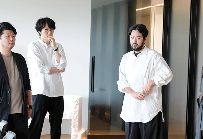 A photo of Yuya Nakata in a conference room going over the uniforms. Oki Sato and Japan Pavilion staff members listen.